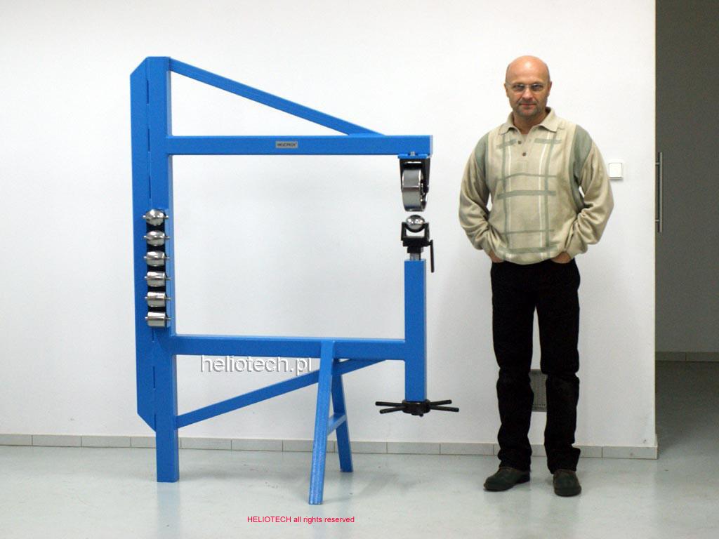 A complete English wheel in blue, with a man standing next to it. A comparison of the size of a rolling mill and a man